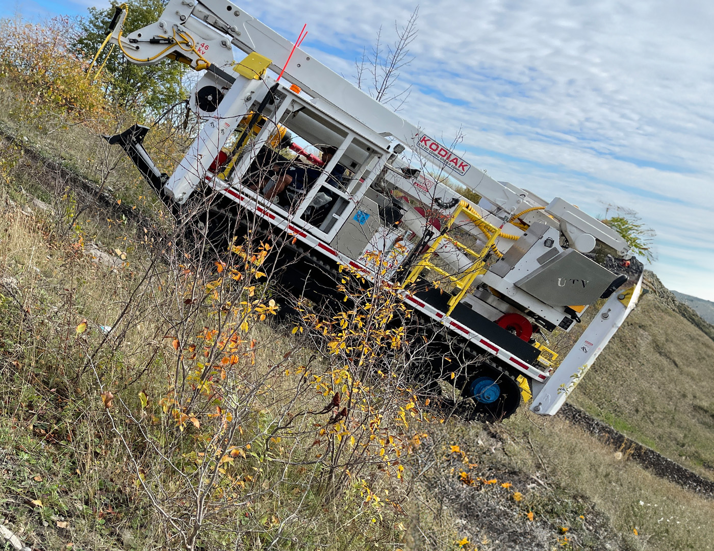 UTV tracked carrier climbing a steep grassy slope with utility boom deployed